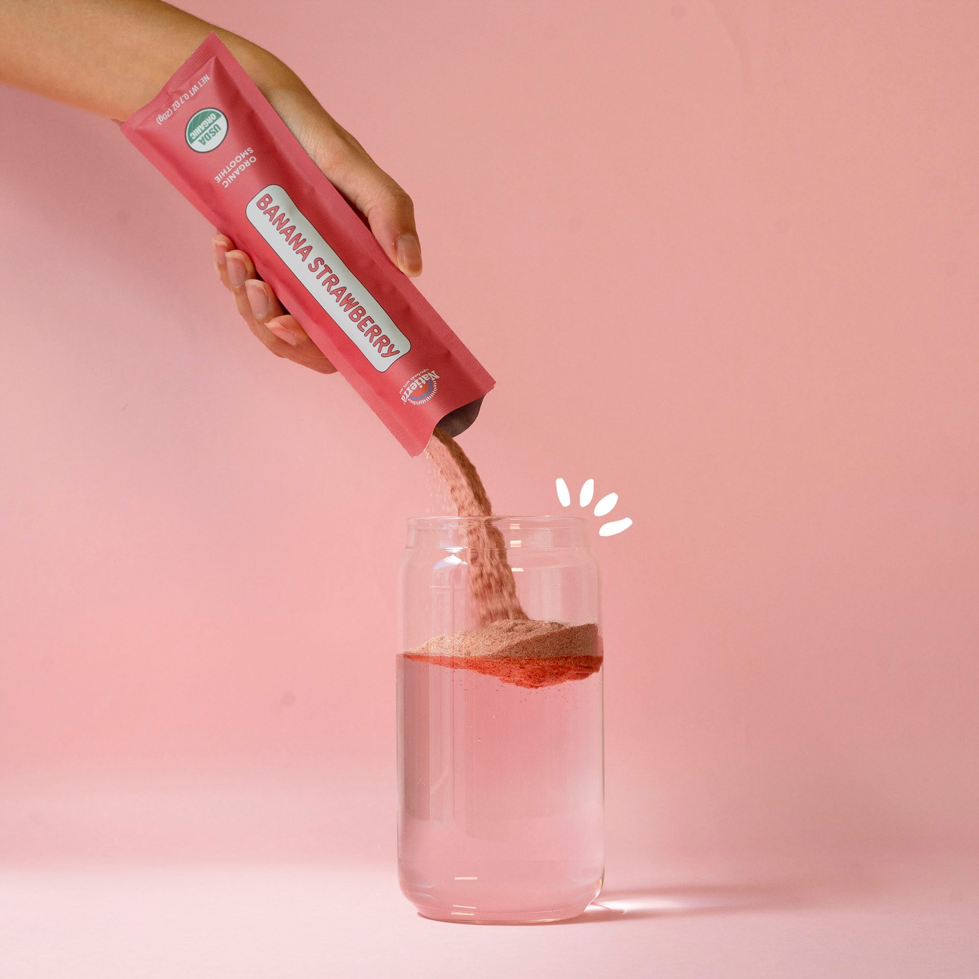 organic banana strawberry smoothie packet being poured into a glass of water