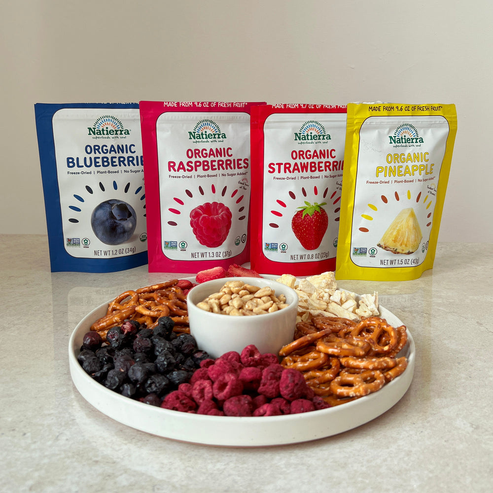 Organic freeze-dried fruit bags of blueberries, raspberries, strawberries and pineapples with a plate of freeze-dried snacks, peanuts and pretzels