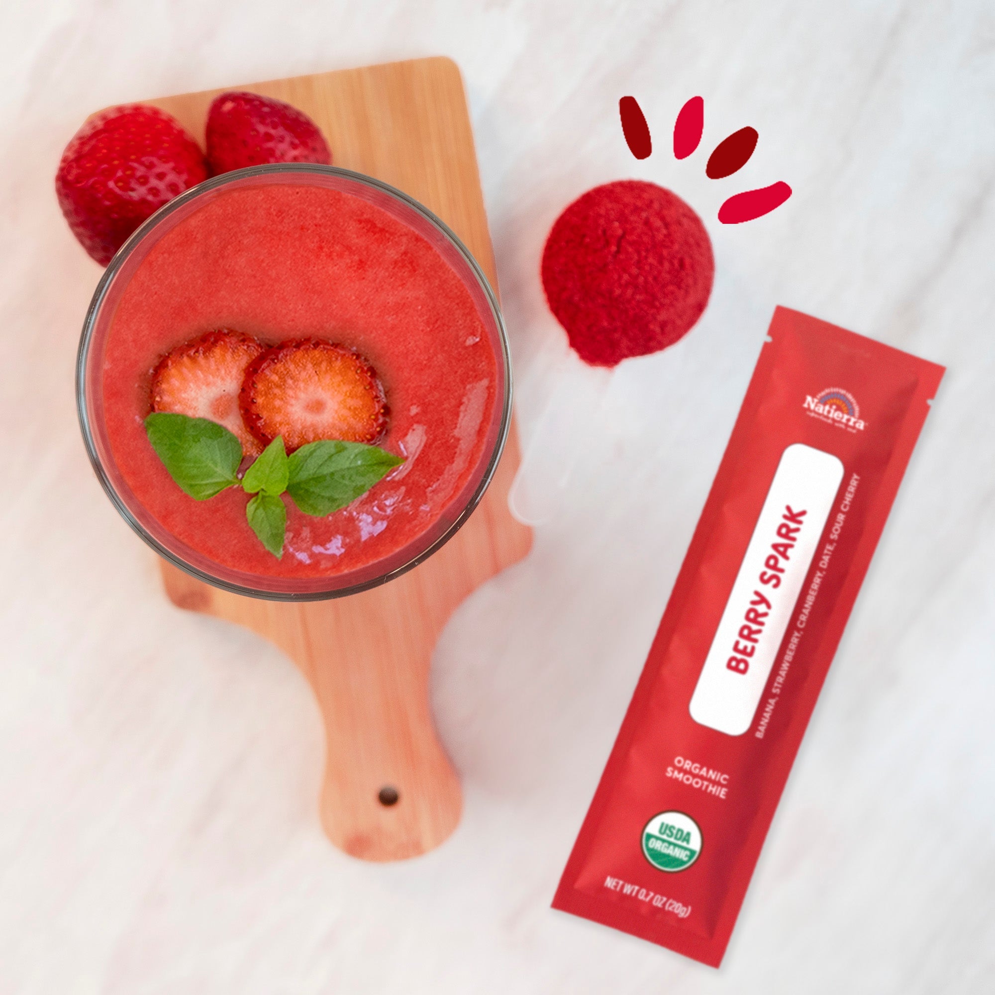Smoothie in a glass on a counter next to a Berry Spark smoothie packet and fresh strawberries
