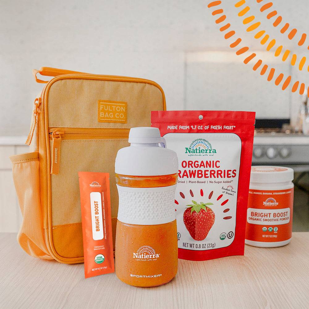 Smoothie shaker with bright boost smoothie packet and jar, and freeze-dried strawberries next to a lunchbox