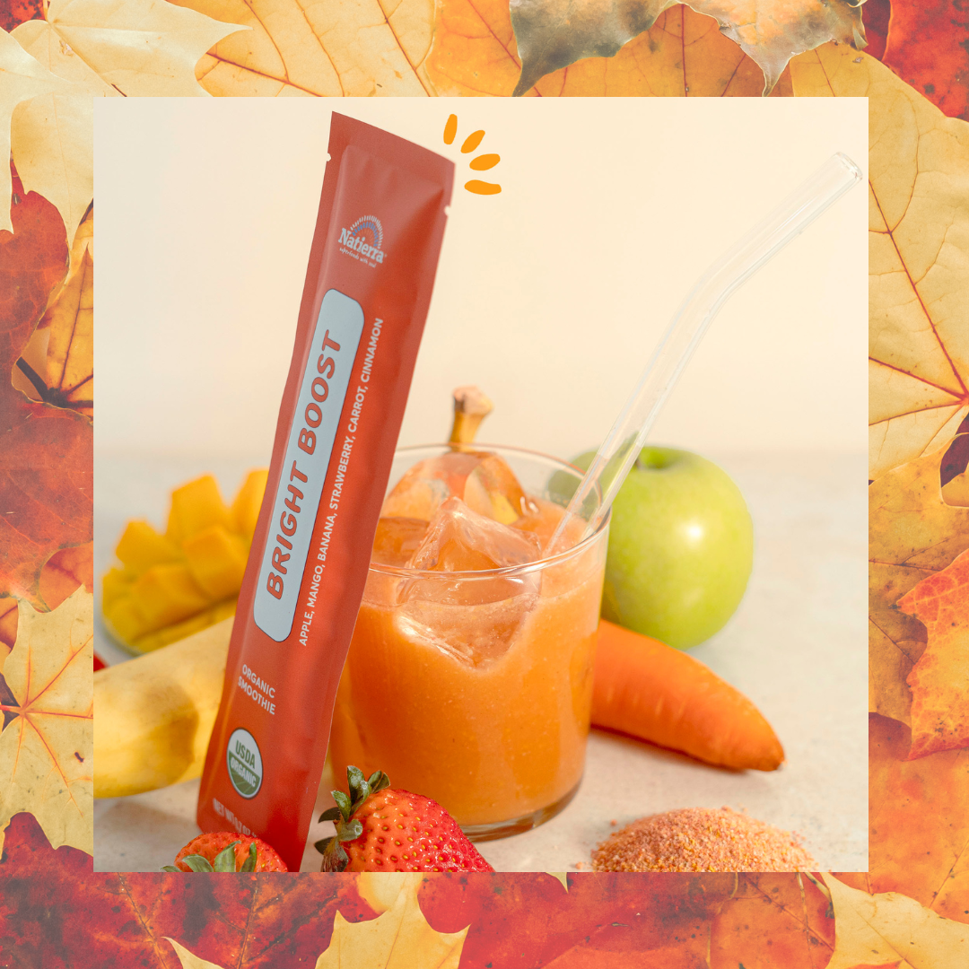 Organic bright boost smoothie powder next to a glass of smoothie liquid on a background of orange leaves