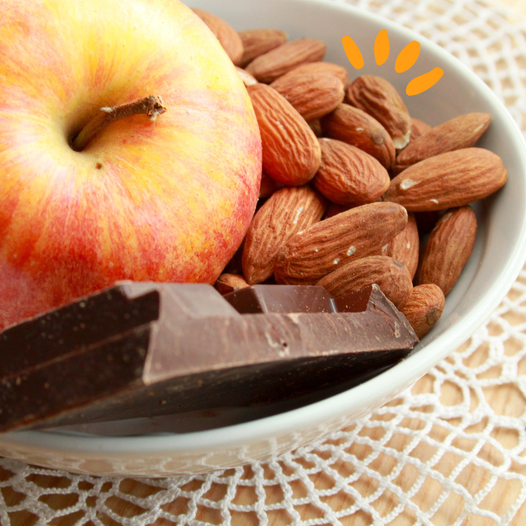 An apple, almonds and a piece of chocolate in a bowl 
