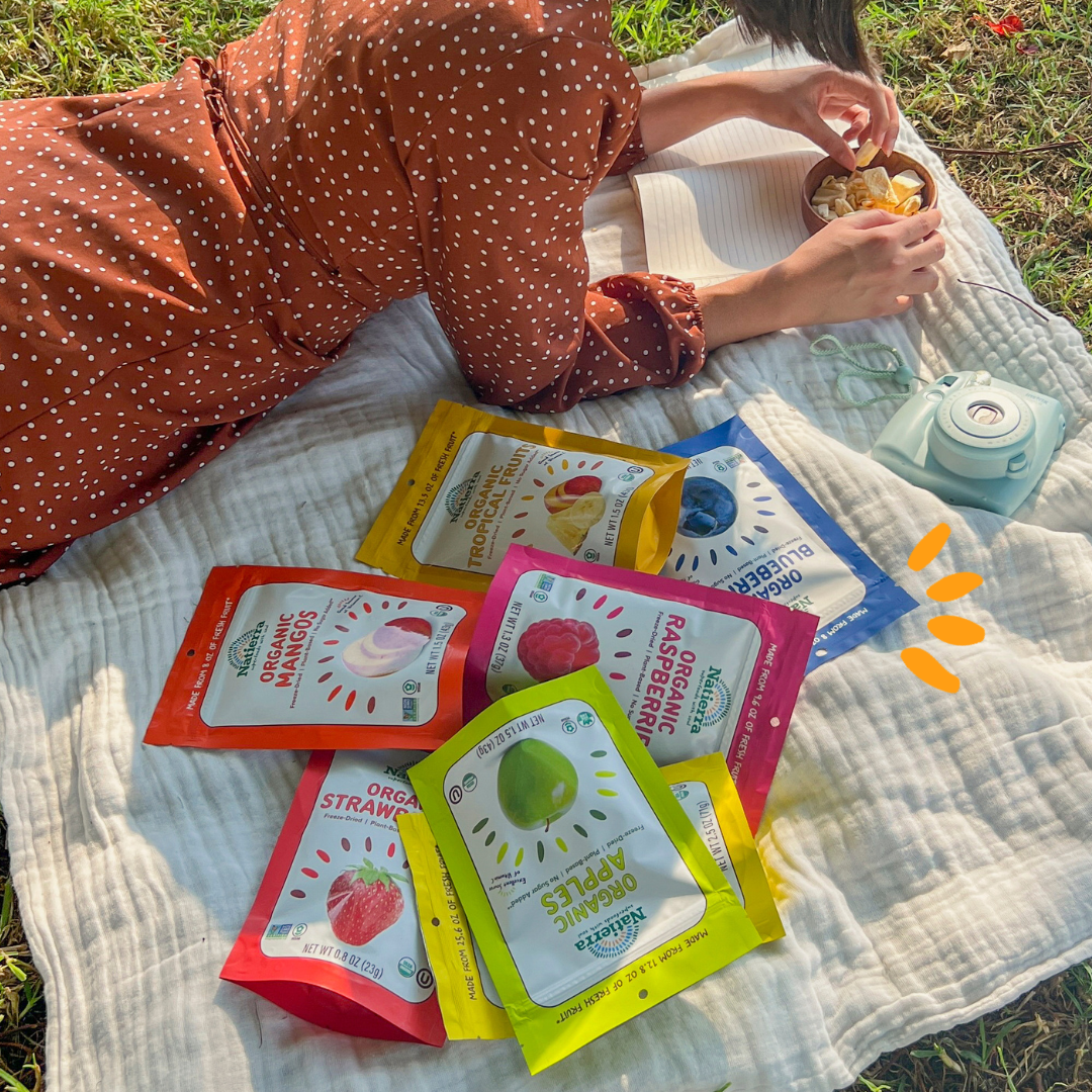 A girl lying on the grass on top of a blanket with freeze-dried fruit snack bags