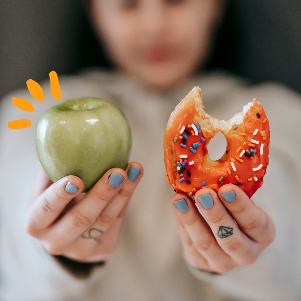 A women holding one fresh apple in one hand and a donut in the other