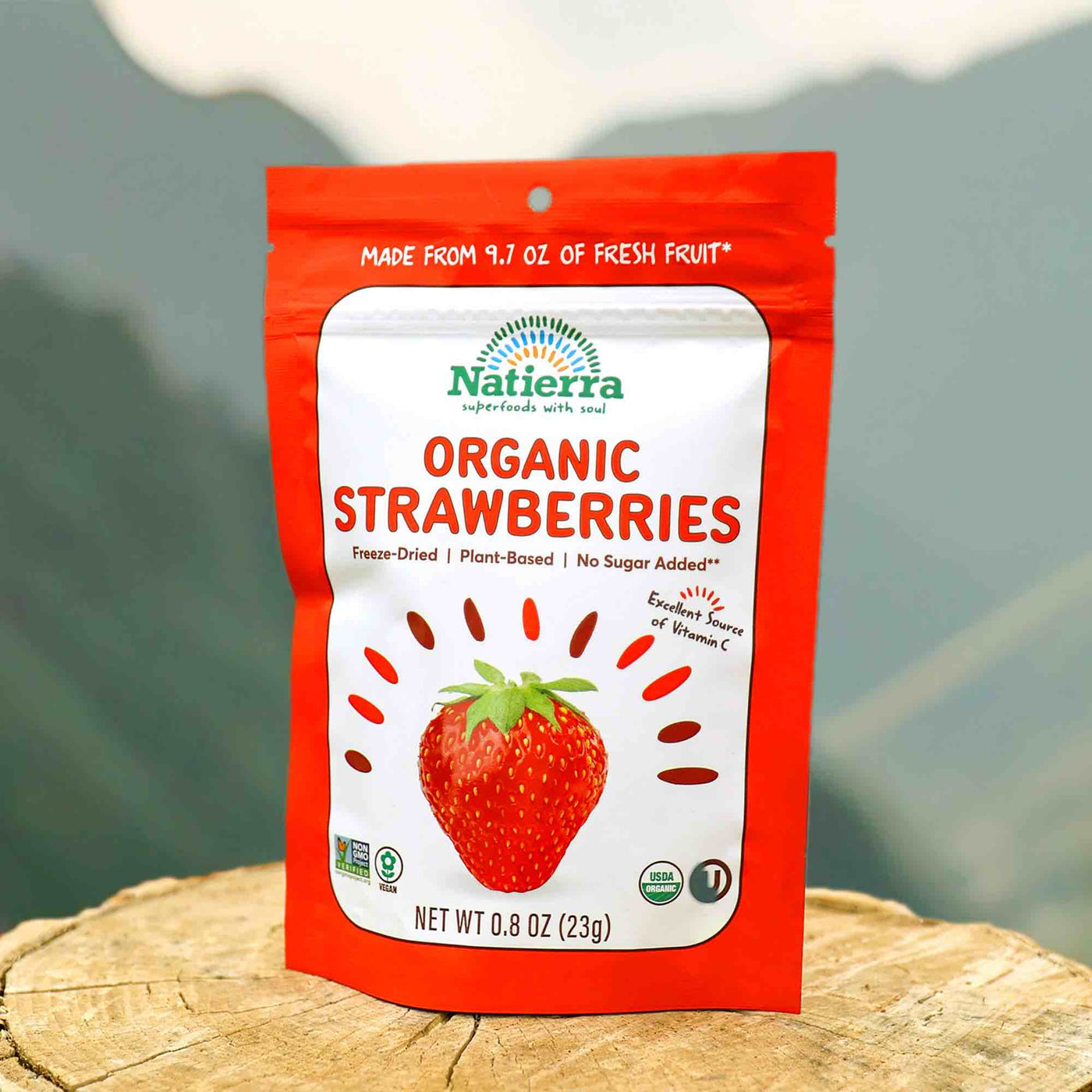 Bag of Natierra's organic freeze dried strawberries on a log in front of a mountain background