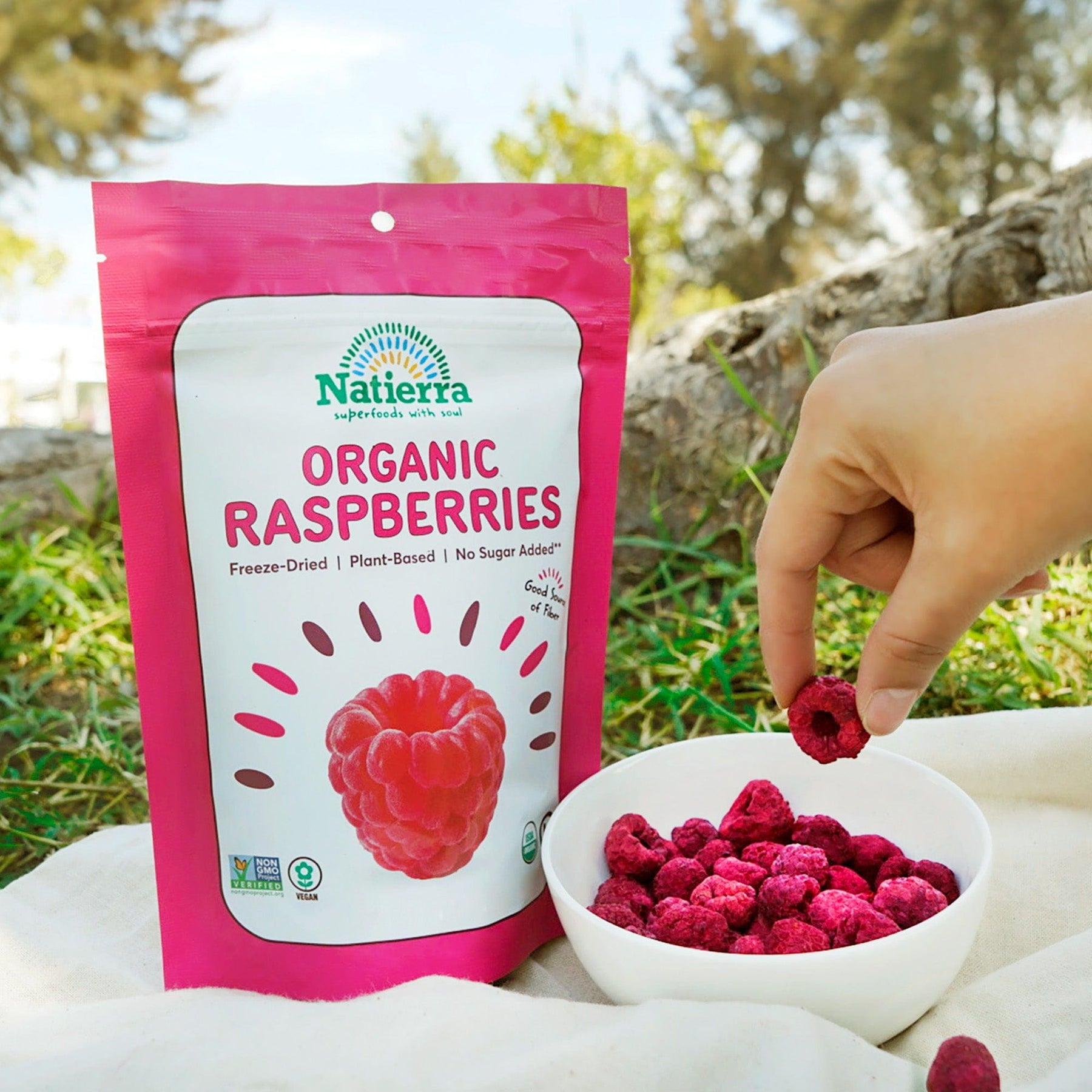 A hand picking up Natierra Organic Raspberries from a bowl. 